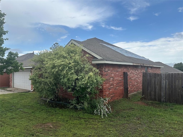 view of home's exterior with fence, a yard, roof with shingles, and brick siding