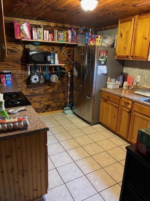 kitchen with freestanding refrigerator, light tile patterned flooring, black microwave, and wood ceiling