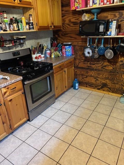 kitchen with open shelves, black microwave, gas range, brown cabinets, and light tile patterned floors
