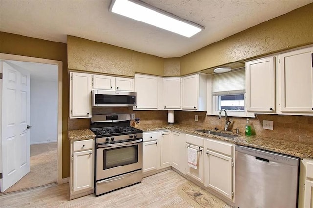 1904 NW Euclid Ave, Lawton, OK 73507 - kitchen featuring light wood-style floors, white cabinets, a sink, backsplash, and stainless steel appliances