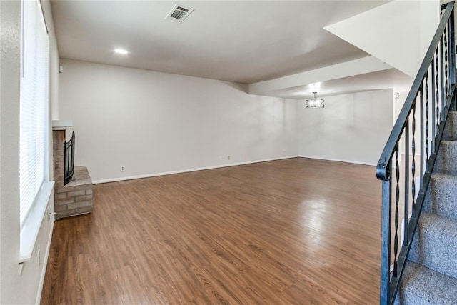unfurnished living room featuring stairs, dark wood-style flooring, visible vents, and a brick fireplace