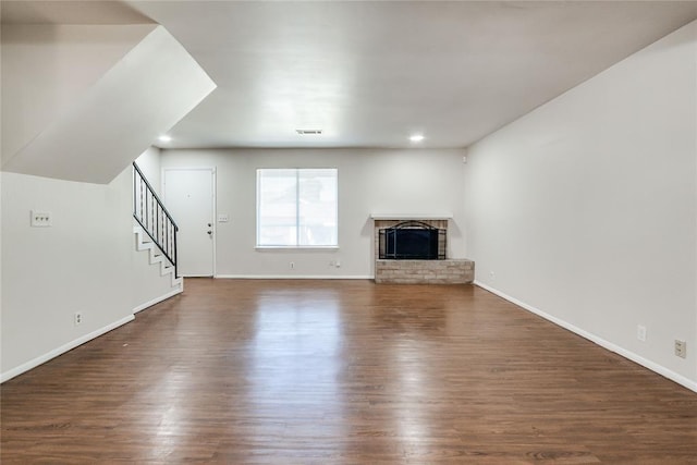unfurnished living room with visible vents, stairs, a fireplace, baseboards, and dark wood-style floors