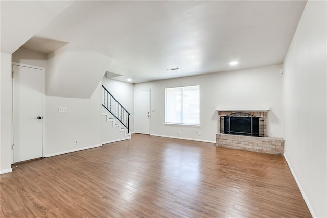 unfurnished living room with a brick fireplace, wood finished floors, stairway, baseboards, and recessed lighting