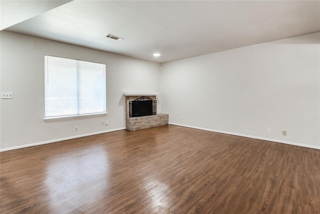 unfurnished living room featuring a brick fireplace, visible vents, and dark wood-type flooring