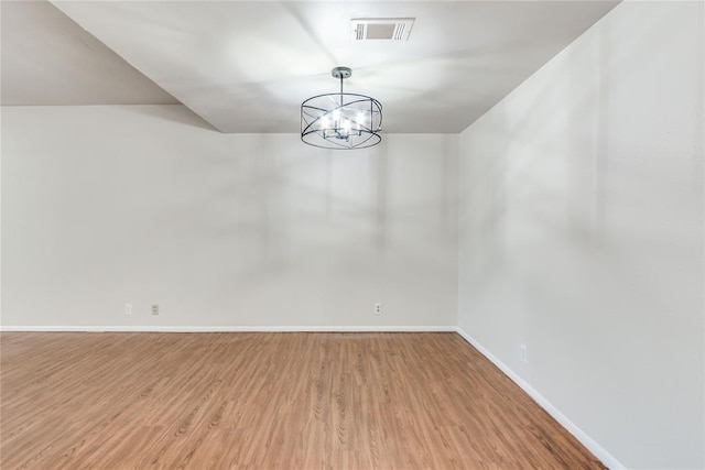 unfurnished room featuring an inviting chandelier, baseboards, wood finished floors, and visible vents