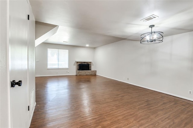 unfurnished living room with visible vents, a fireplace, baseboards, dark wood-style floors, and an inviting chandelier