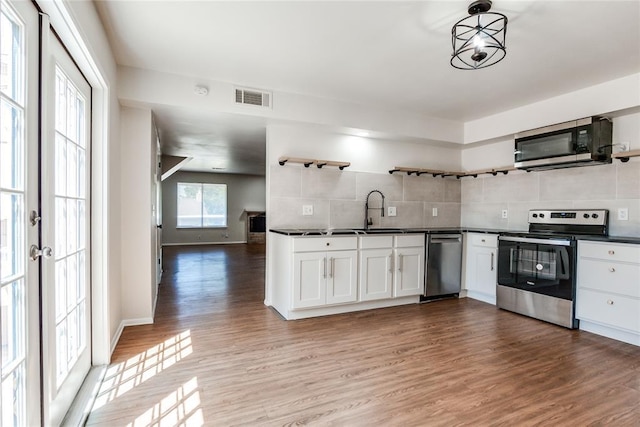 kitchen with open shelves, decorative backsplash, dark countertops, a sink, and stainless steel appliances