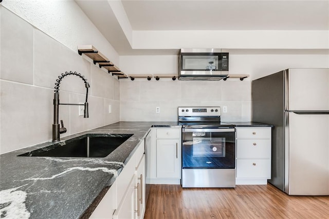 kitchen with decorative backsplash, open shelves, a sink, stainless steel appliances, and white cabinetry