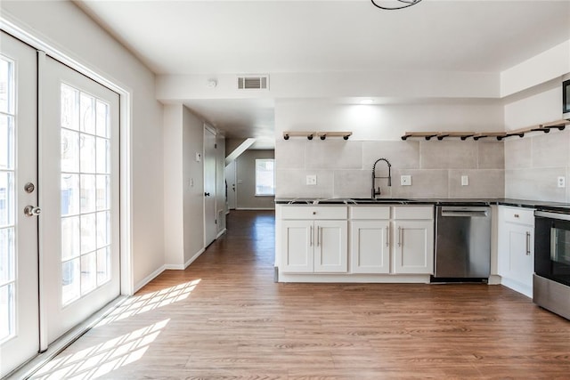kitchen featuring open shelves, dark countertops, a sink, stainless steel appliances, and visible vents