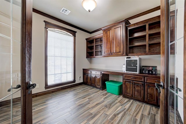 unfurnished office with visible vents, ornamental molding, built in desk, and light wood-style flooring