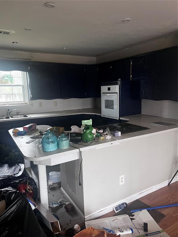 kitchen with dark cabinets, black cooktop, a sink, oven, and visible vents