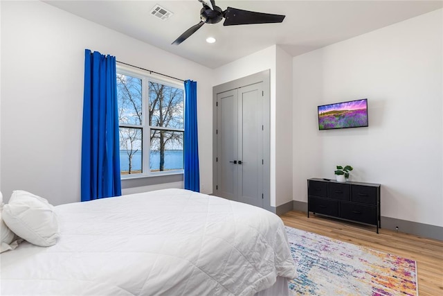 bedroom with visible vents, a closet, wood finished floors, baseboards, and ceiling fan