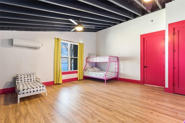 bedroom with baseboards, a wall mounted AC, and wood finished floors