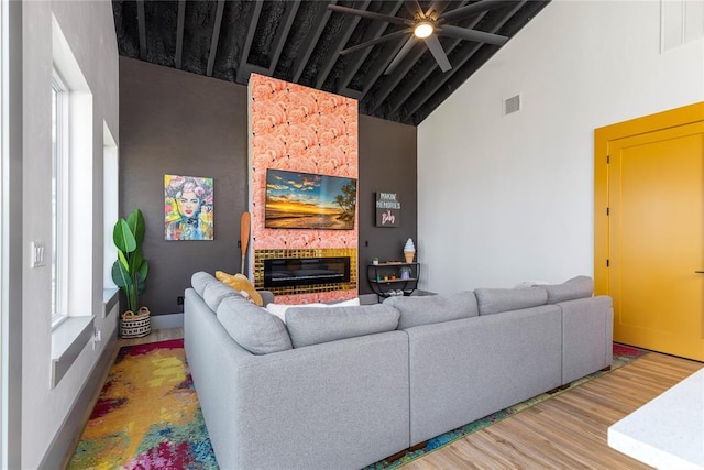 living room featuring a ceiling fan, visible vents, a brick fireplace, wood finished floors, and high vaulted ceiling