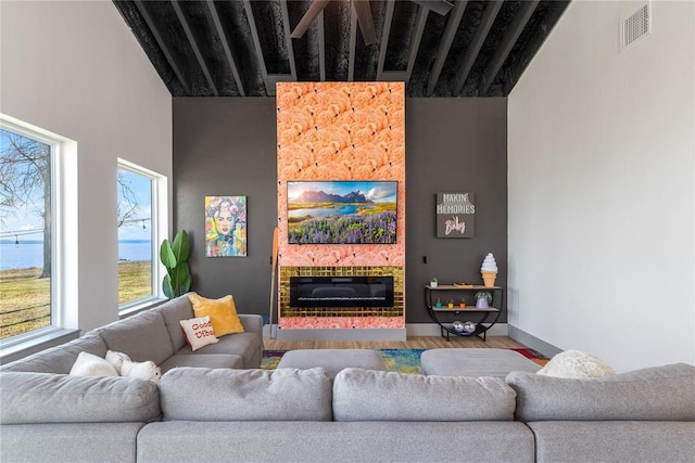 living area featuring visible vents, plenty of natural light, wood finished floors, and a glass covered fireplace