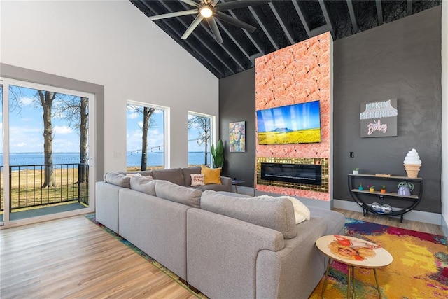 living area with light wood-style floors, ceiling fan, high vaulted ceiling, a water view, and a large fireplace