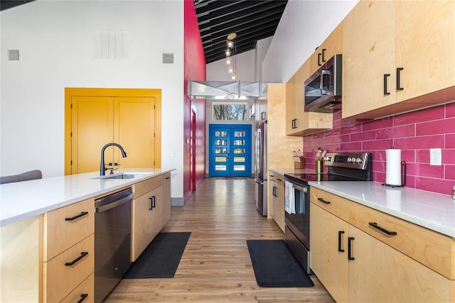 kitchen featuring light brown cabinetry, appliances with stainless steel finishes, a sink, decorative backsplash, and a towering ceiling