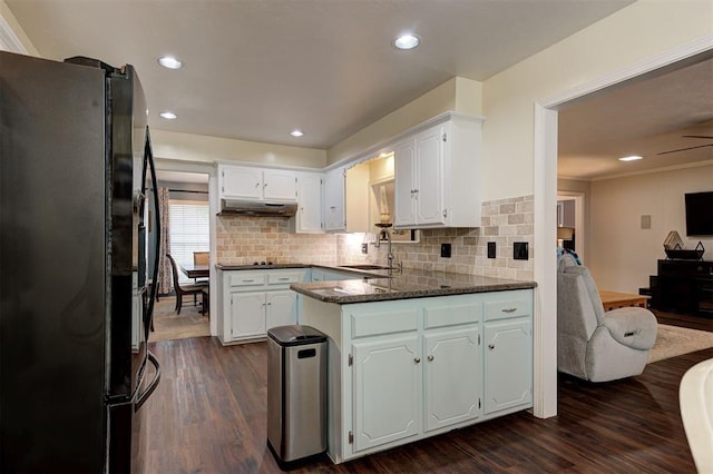 kitchen featuring a sink, freestanding refrigerator, a peninsula, under cabinet range hood, and dark wood-style floors