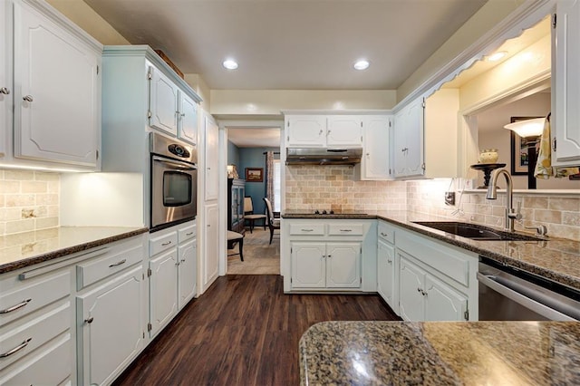 kitchen featuring dark wood-style floors, under cabinet range hood, a sink, appliances with stainless steel finishes, and backsplash