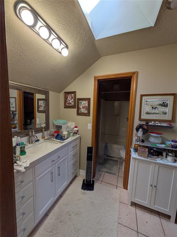 900 Walnut Pl, Norman, OK 73072 - bathroom with a textured ceiling, vaulted ceiling, a skylight, vanity, and tile patterned flooring