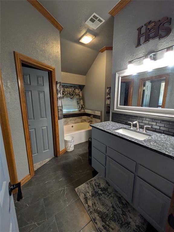 900 Walnut Pl, Norman, OK 73072 - bathroom with lofted ceiling, a textured wall, vanity, and a garden tub