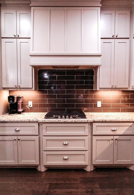 kitchen with decorative backsplash, black cooktop, dark wood-style floors, and light stone counters