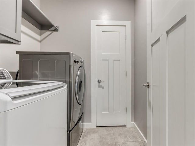clothes washing area featuring cabinet space, light tile patterned floors, baseboards, and washer and clothes dryer