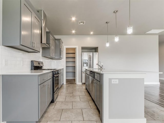 kitchen featuring decorative backsplash, an island with sink, gray cabinets, appliances with stainless steel finishes, and light tile patterned floors