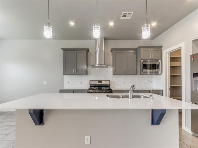 kitchen with light tile patterned flooring, wall chimney range hood, a sink, gray cabinetry, and stainless steel appliances