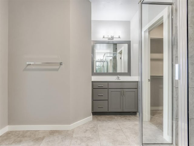 bathroom featuring baseboards, vanity, tile patterned floors, and a walk in closet