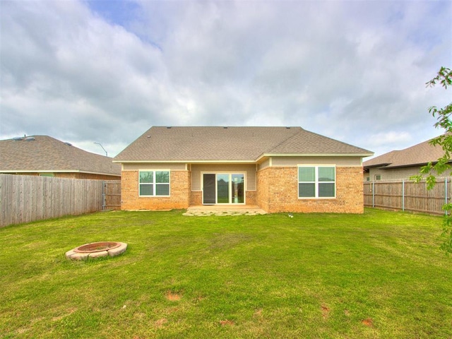 rear view of house featuring brick siding, a fenced backyard, an outdoor fire pit, and a yard