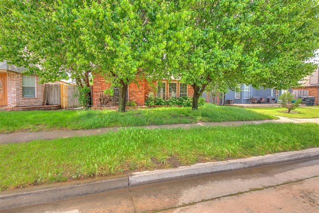 view of property hidden behind natural elements with fence and brick siding