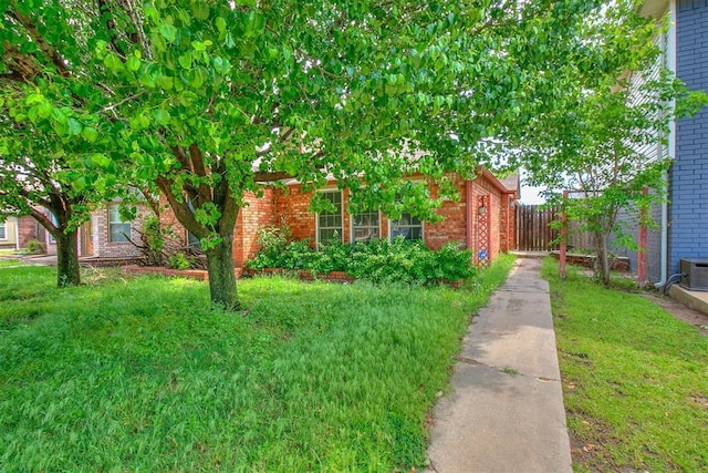 view of property hidden behind natural elements featuring brick siding, fence, and a front yard
