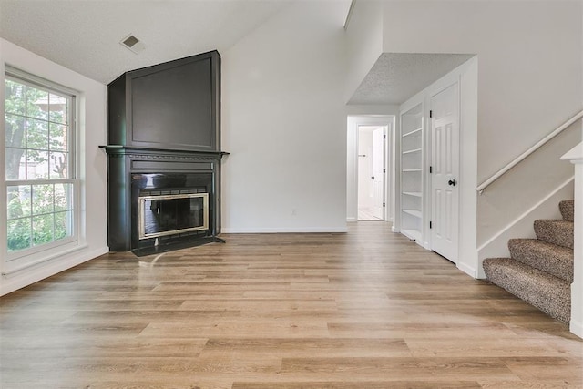 unfurnished living room with visible vents, a large fireplace, vaulted ceiling, light wood-style floors, and stairs