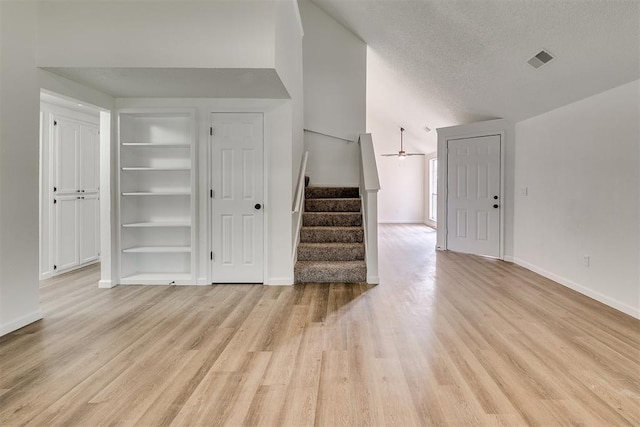 unfurnished living room with stairs, baseboards, built in shelves, and light wood-style flooring