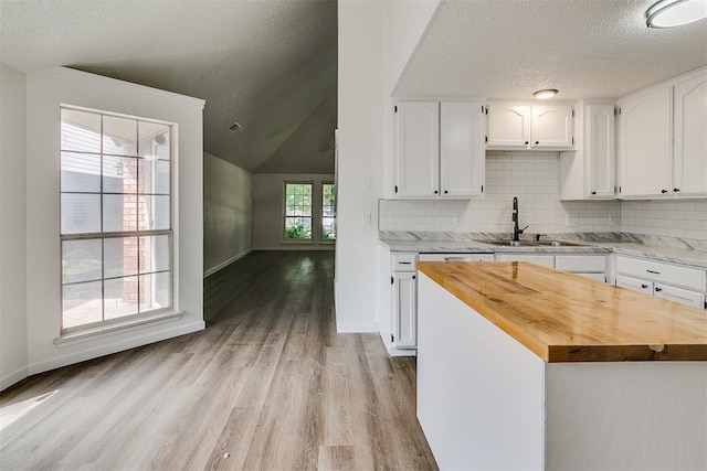 kitchen with a sink, a textured ceiling, wooden counters, and white cabinetry