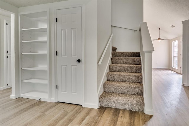 stairs with baseboards, a ceiling fan, built in features, and wood finished floors