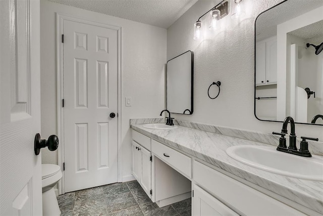 bathroom featuring double vanity, toilet, a textured ceiling, and a sink
