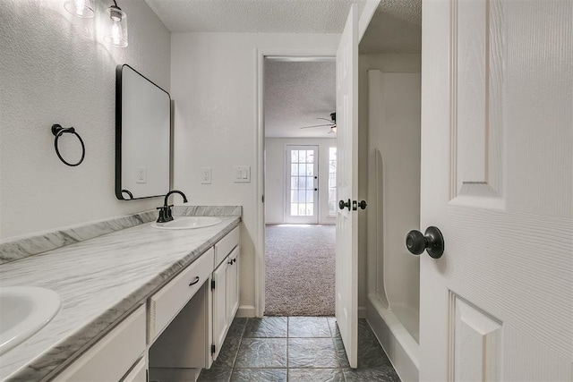 full bathroom with double vanity, ceiling fan, a textured ceiling, walk in shower, and a sink