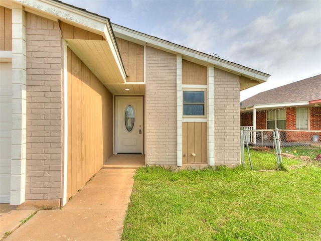 entrance to property featuring brick siding, fence, and a yard