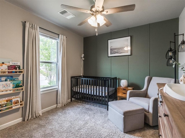 bedroom featuring visible vents, carpet floors, baseboards, a crib, and a ceiling fan