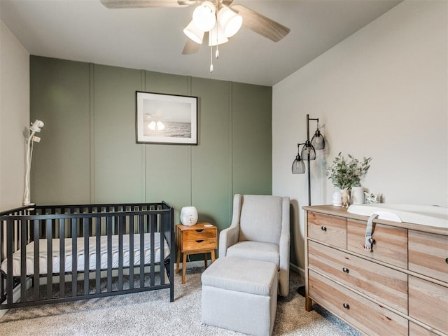 carpeted bedroom featuring a ceiling fan, a crib, and a decorative wall
