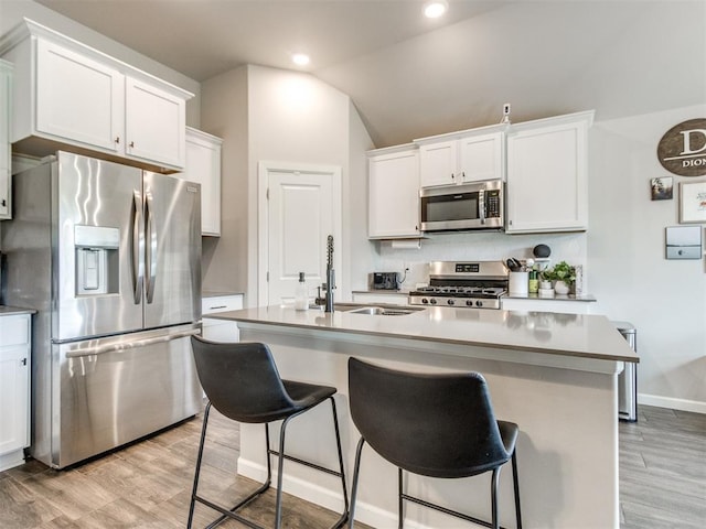 kitchen with appliances with stainless steel finishes, a sink, light wood-style flooring, and a kitchen bar