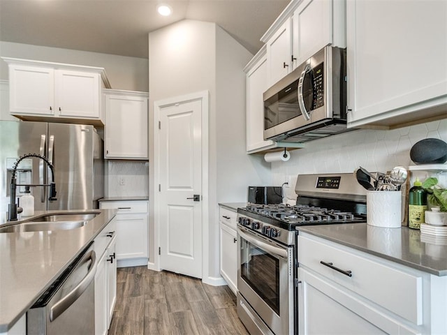 kitchen with backsplash, stainless steel appliances, wood finished floors, and white cabinetry
