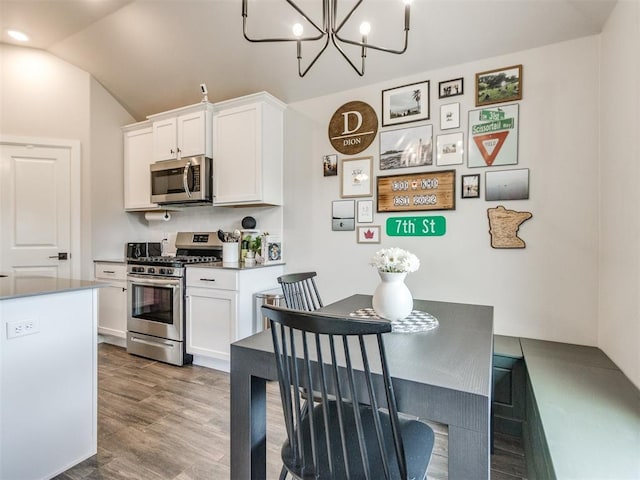 kitchen with white cabinets, appliances with stainless steel finishes, a chandelier, wood finished floors, and vaulted ceiling