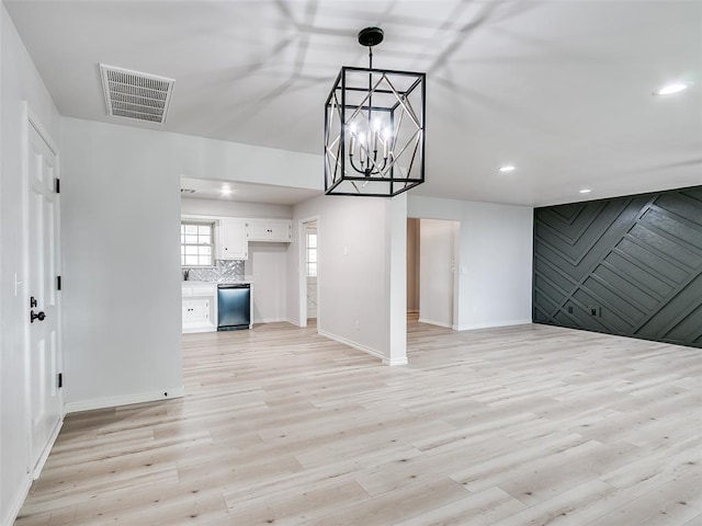 unfurnished living room featuring visible vents, light wood finished floors, baseboards, and an inviting chandelier