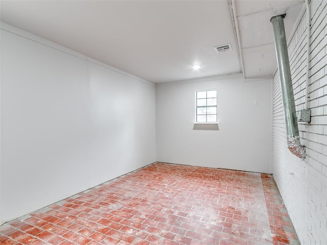 spare room with brick floor, ornamental molding, and visible vents
