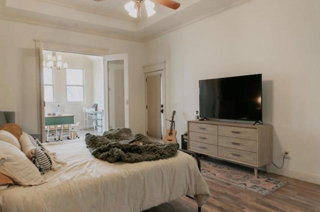 bedroom featuring wood finished floors, a raised ceiling, baseboards, ceiling fan with notable chandelier, and ornamental molding