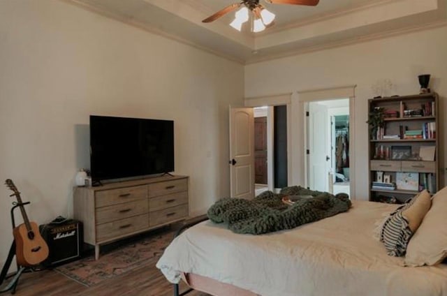 bedroom with ornamental molding, a tray ceiling, dark wood finished floors, and ceiling fan