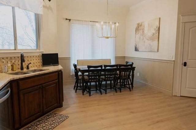 dining room featuring a healthy amount of sunlight, wainscoting, light wood-type flooring, and a notable chandelier